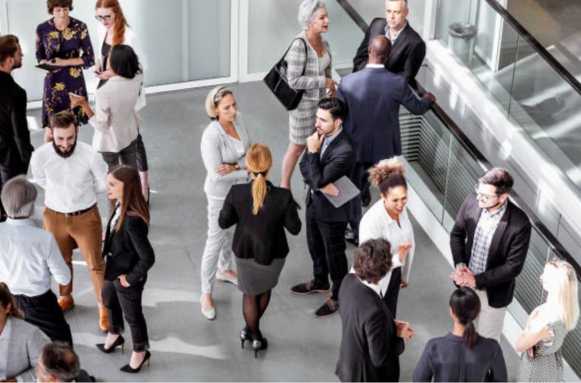Large group of business professionals engaged in conversations and networking in a spacious, modern office building.